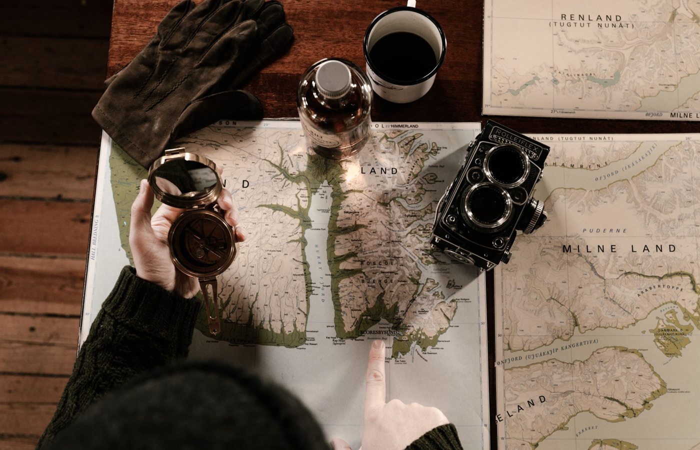 Top view of vintage exploration setup with maps, compass, gloves, and retro camera.