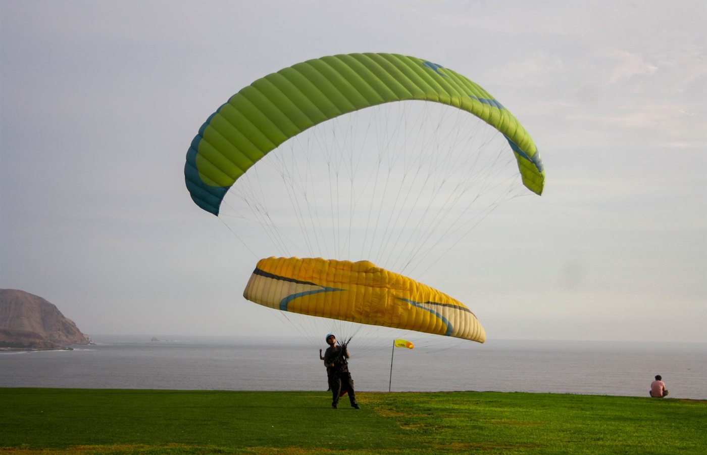 Paraglider landing on a grassy coastal cliff with ocean view, capturing adventure and freedom.